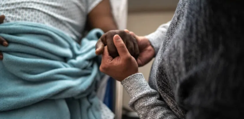 person holding hand of patient in hospital bed